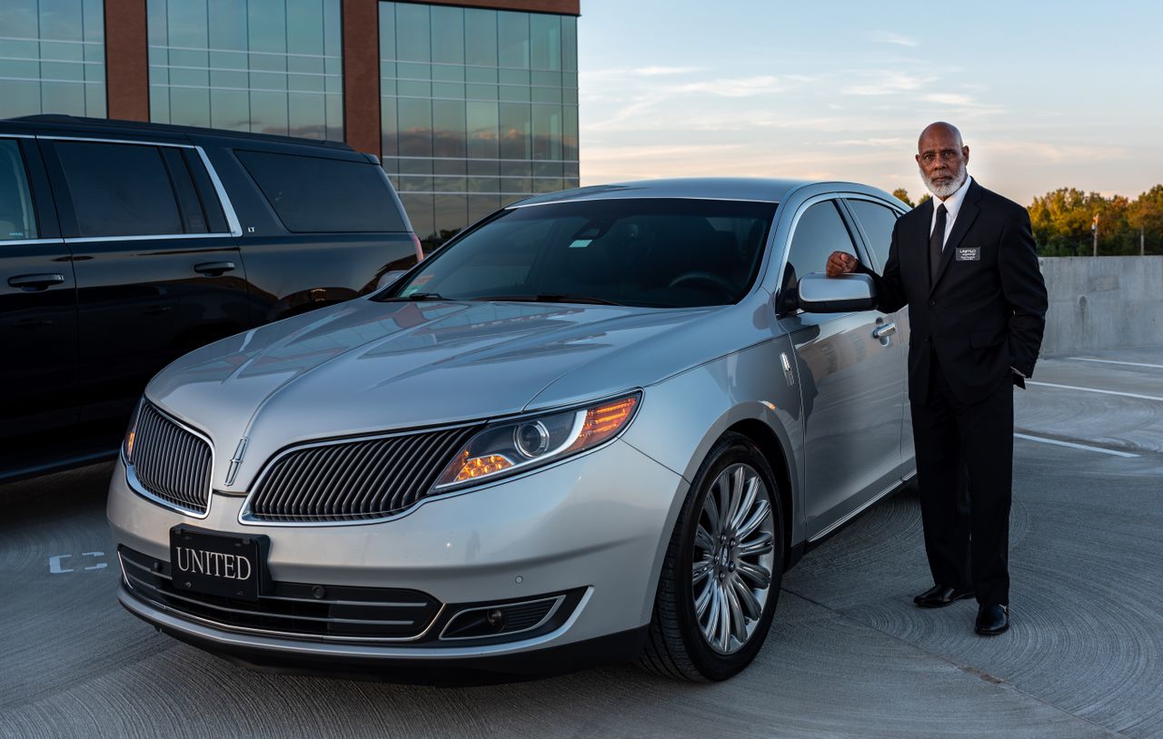 heros-img Professional chauffeur in a suit standing next to a luxury car in outdoor setting.