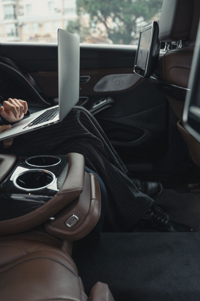 who-we-are A professional woman working remotely on a laptop inside a luxurious car. Modern executive lifestyle.