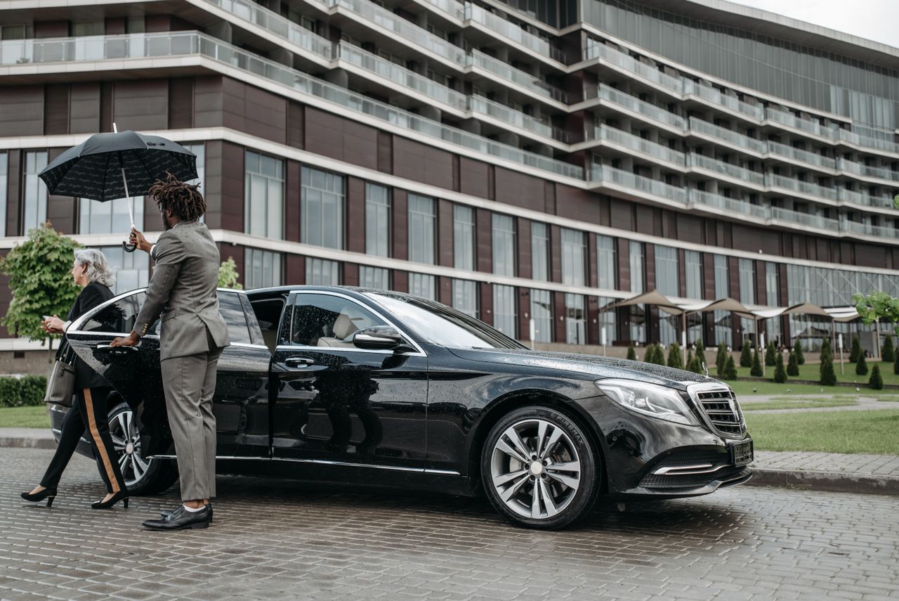 services-01 A business professional exits a luxury car while being shielded by an umbrella.
