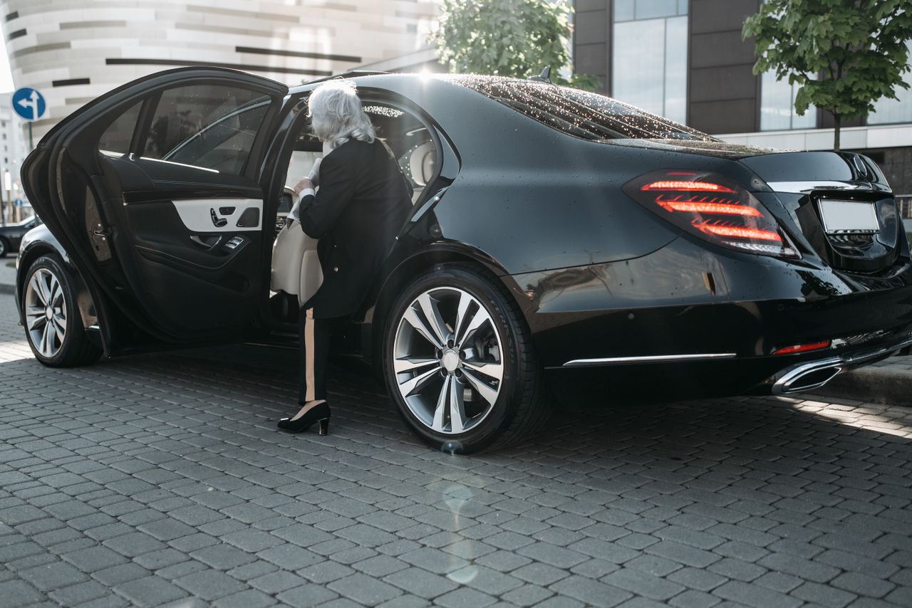 Mastering the First Impression: Your intriguing post title goes here Senior businesswoman stepping out of a sleek black luxury vehicle in a cityscape.